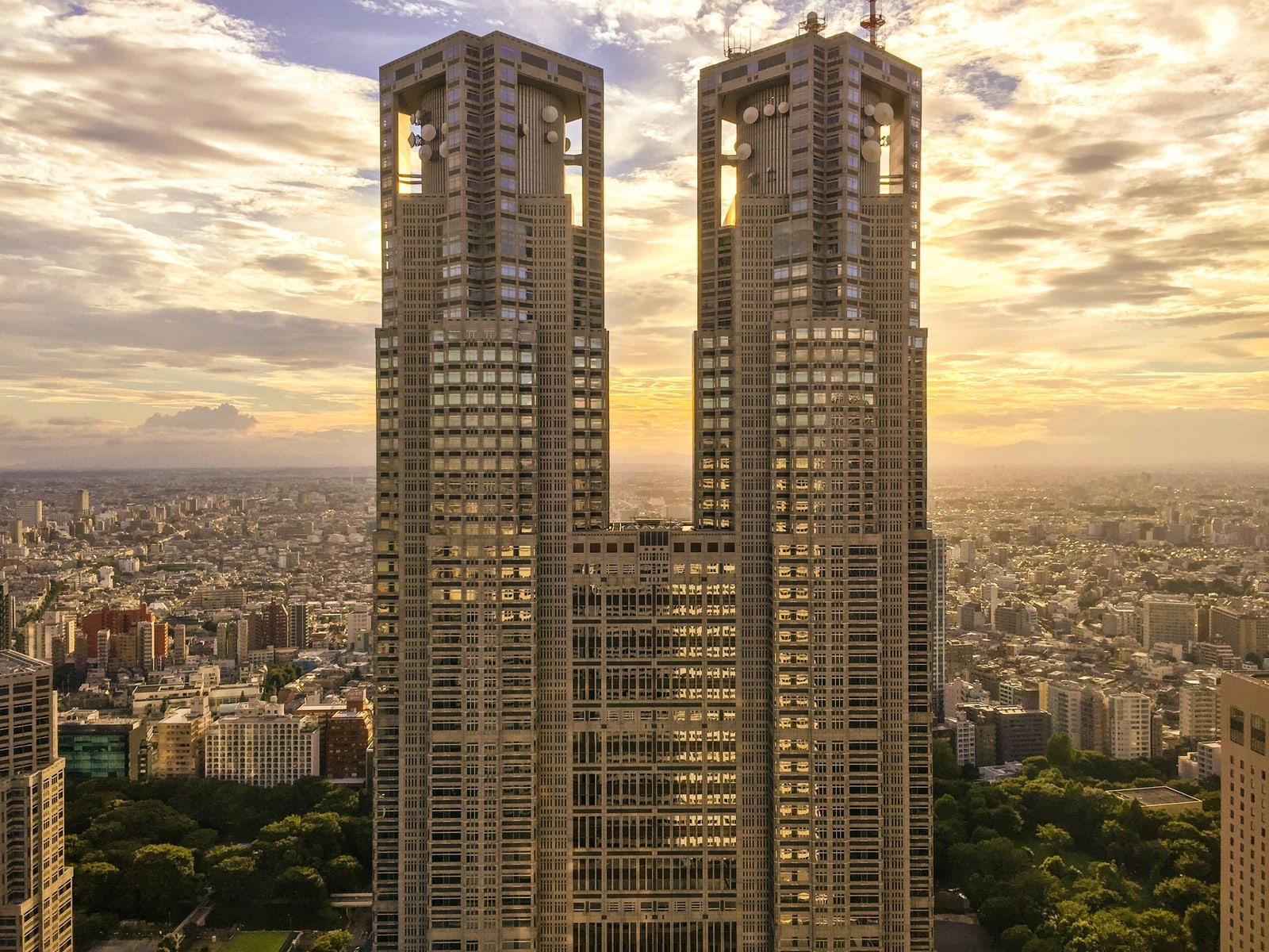 The twin towers of the Tokyo Metropolitan Government Building at sunset, seen from above with the city stretching to the horizon.