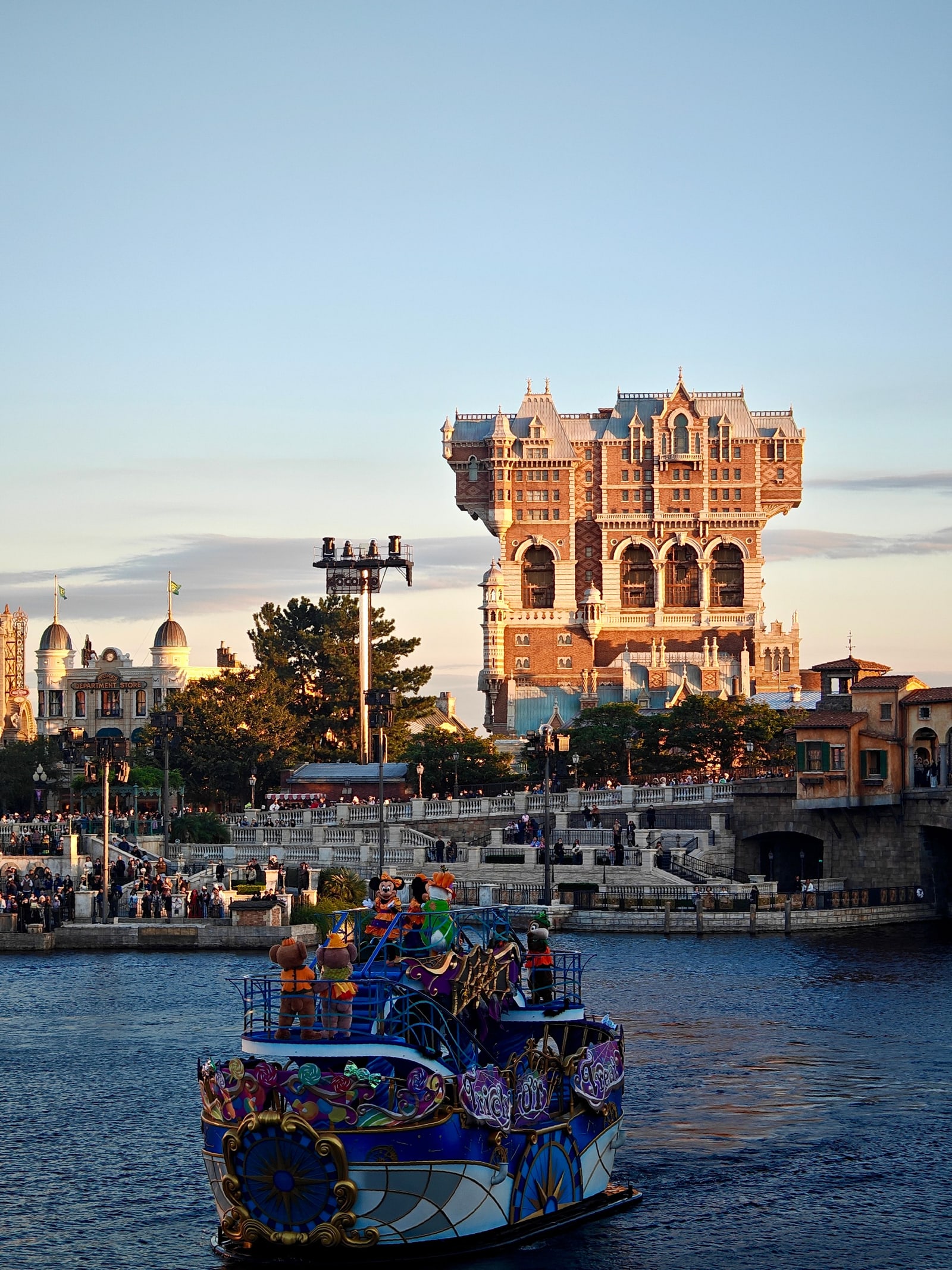 Tokyo DisneySea's Tower of Terror at dusk beyond the harbor, with a costumed parade boat in the foreground.