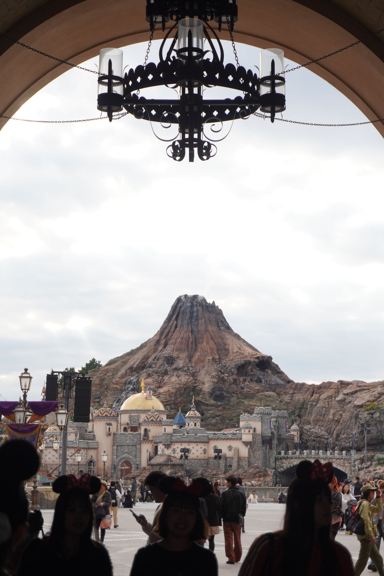 Mount Prometheus, the volcano at Tokyo DisneySea's Mysterious Island, framed under an archway with silhouetted guests in Minnie-ear headbands.