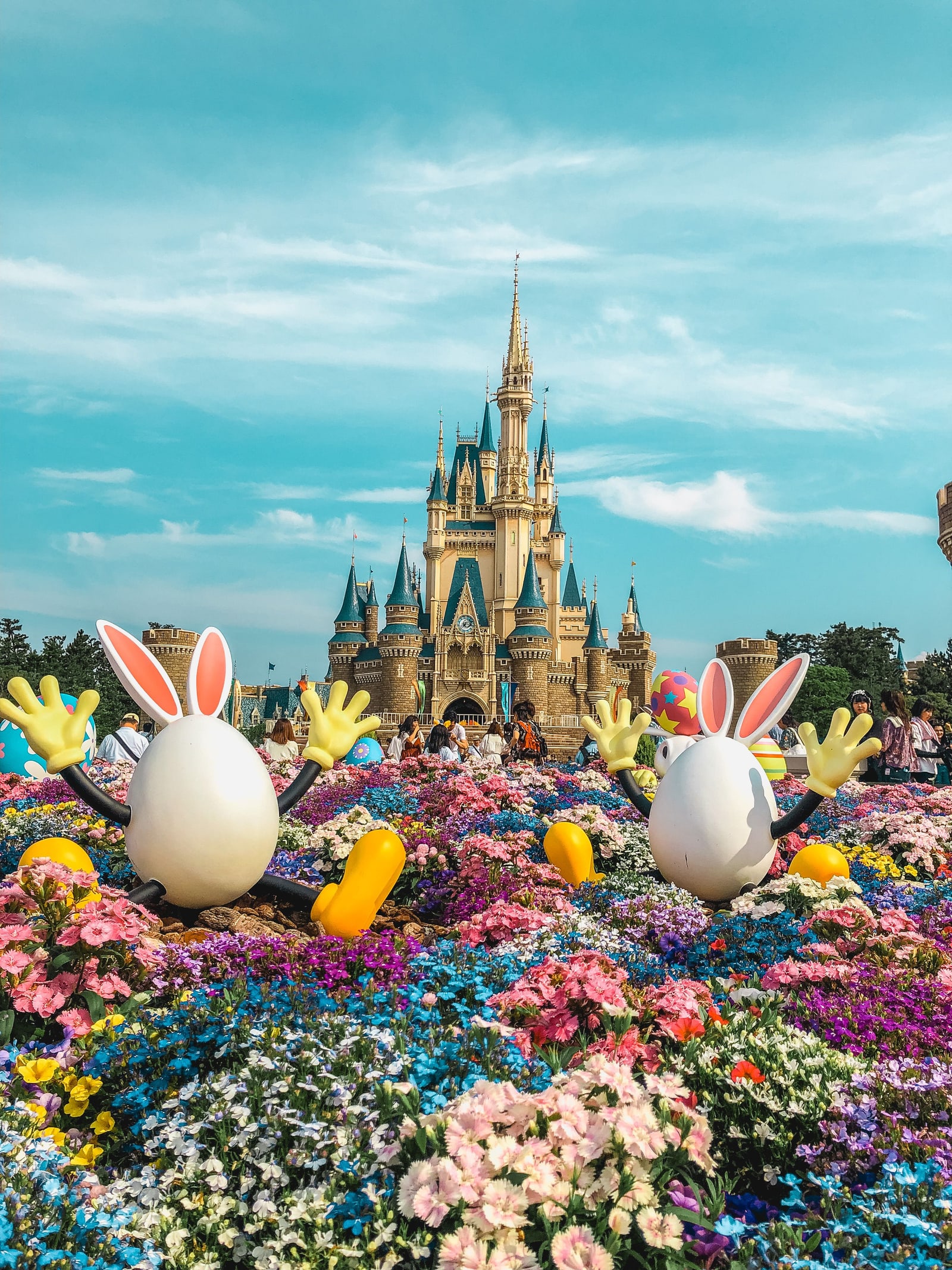 Cinderella Castle at Tokyo Disneyland framed by a springtime Easter flower display with large costumed egg-character props.