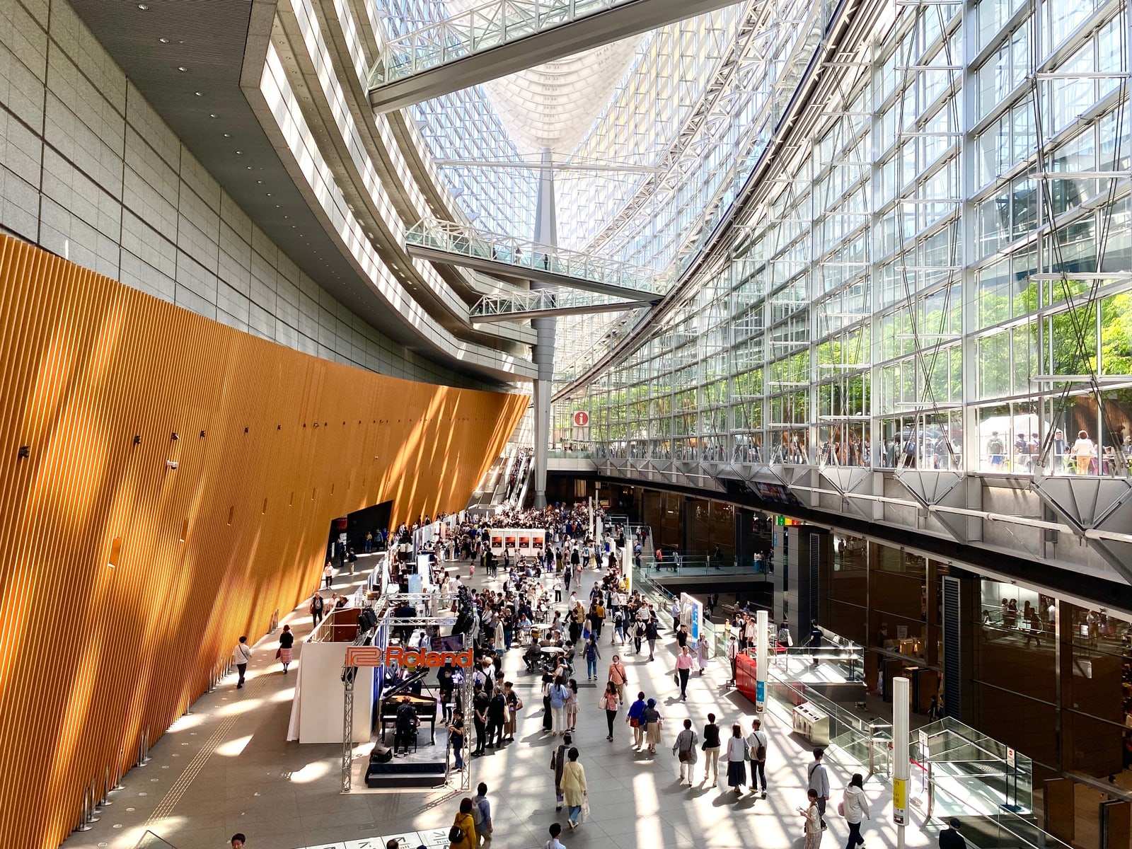 The glass-roofed hall of the Tokyo International Forum seen from an upper level, with glass walkways overhead and visitors crossing the floor