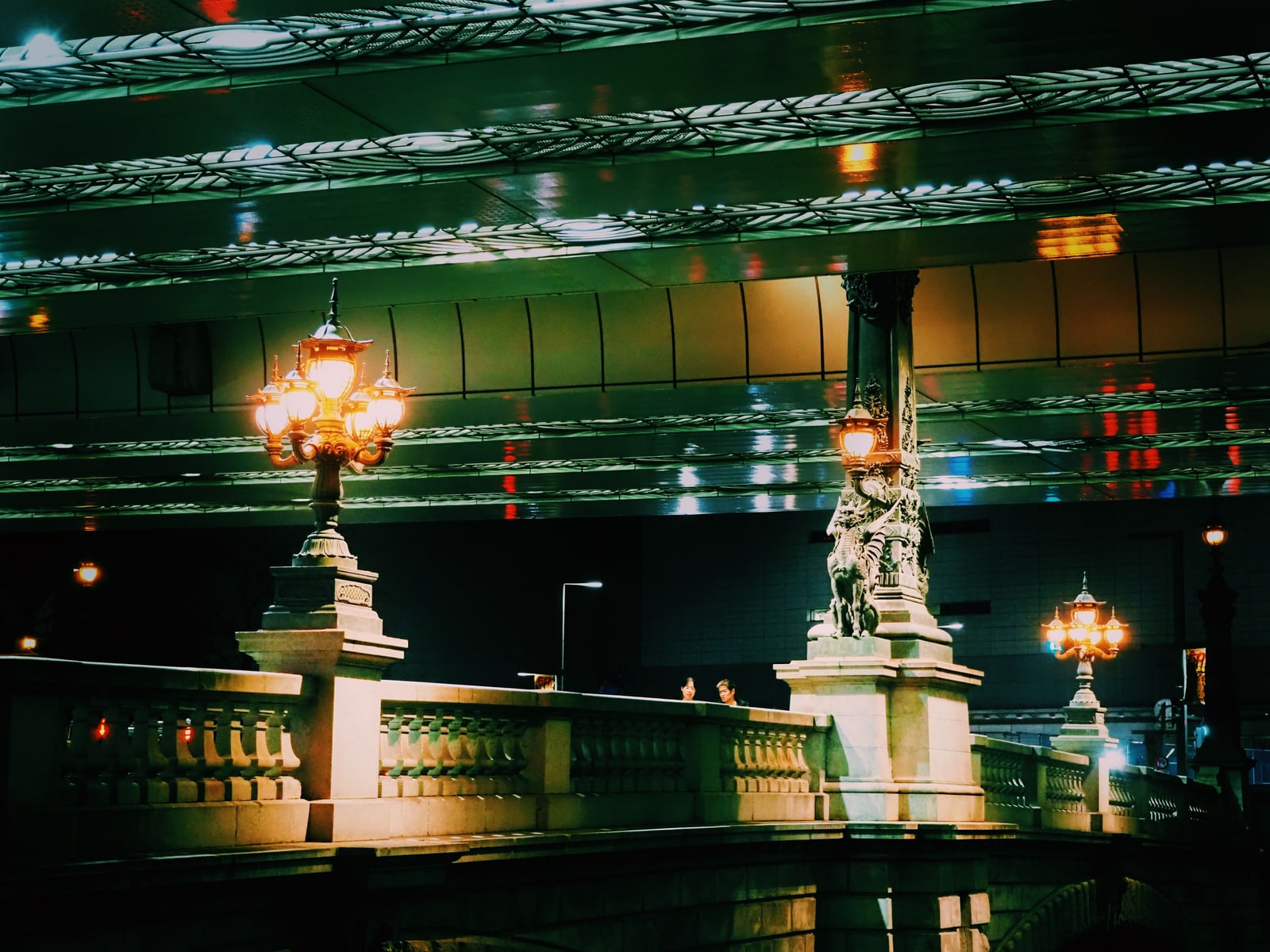Ornate bronze lamp posts and a stone balustrade on the Nihonbashi Bridge at night, the underside of an elevated expressway filling the top of the frame