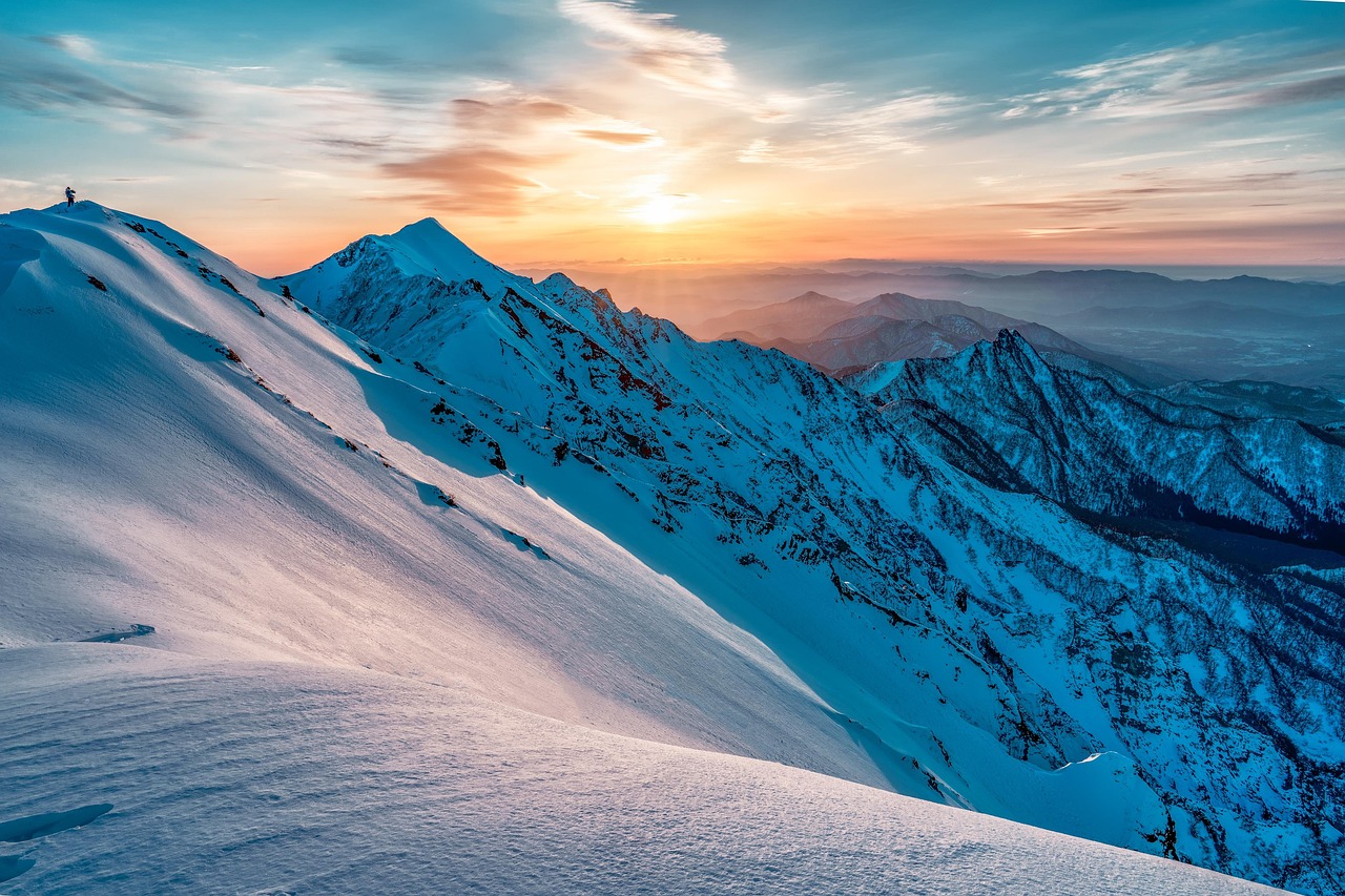 A snow-covered mountain ridge at sunrise, a lone climber on the crest