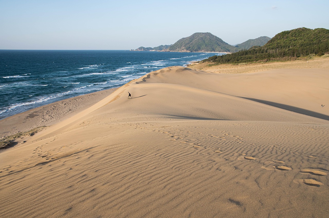 A rippled sand dune dropping to the sea, green hills along the coast beyond