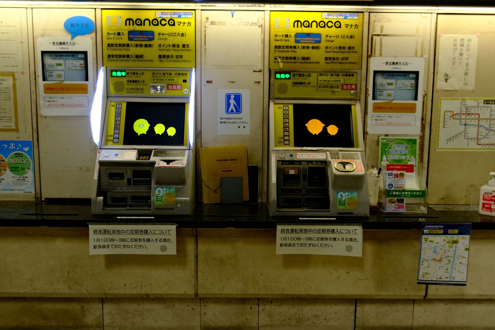 Two subway ticket machines on the Nagoya Municipal Subway, with yellow IC-card panels, Japanese and English menus and posted notices, and nobody in front of them.
