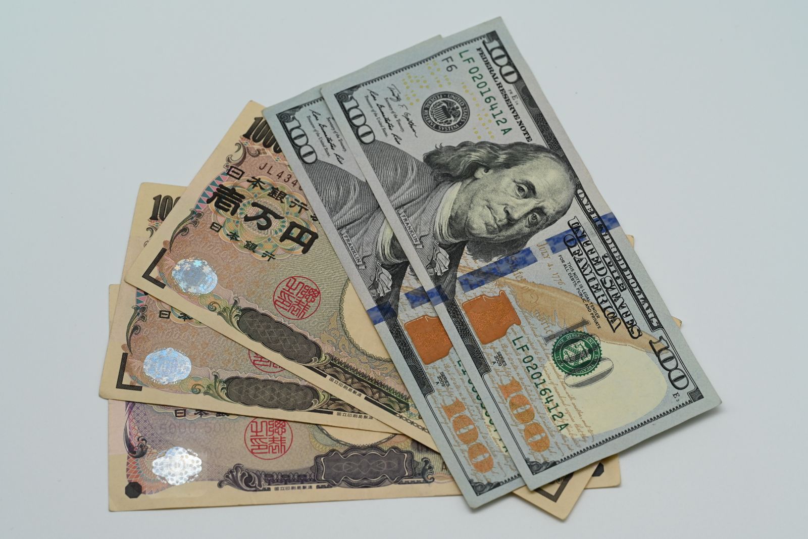 Fanned ten-thousand and five-thousand yen notes under two US hundred-dollar bills on a white surface.