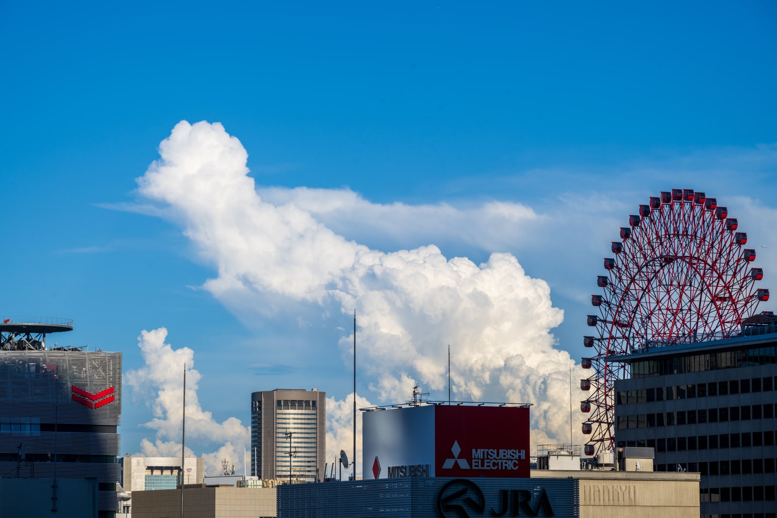A Ferris wheel above Umeda rooftops at the right of the frame, under blue sky and a large cloud