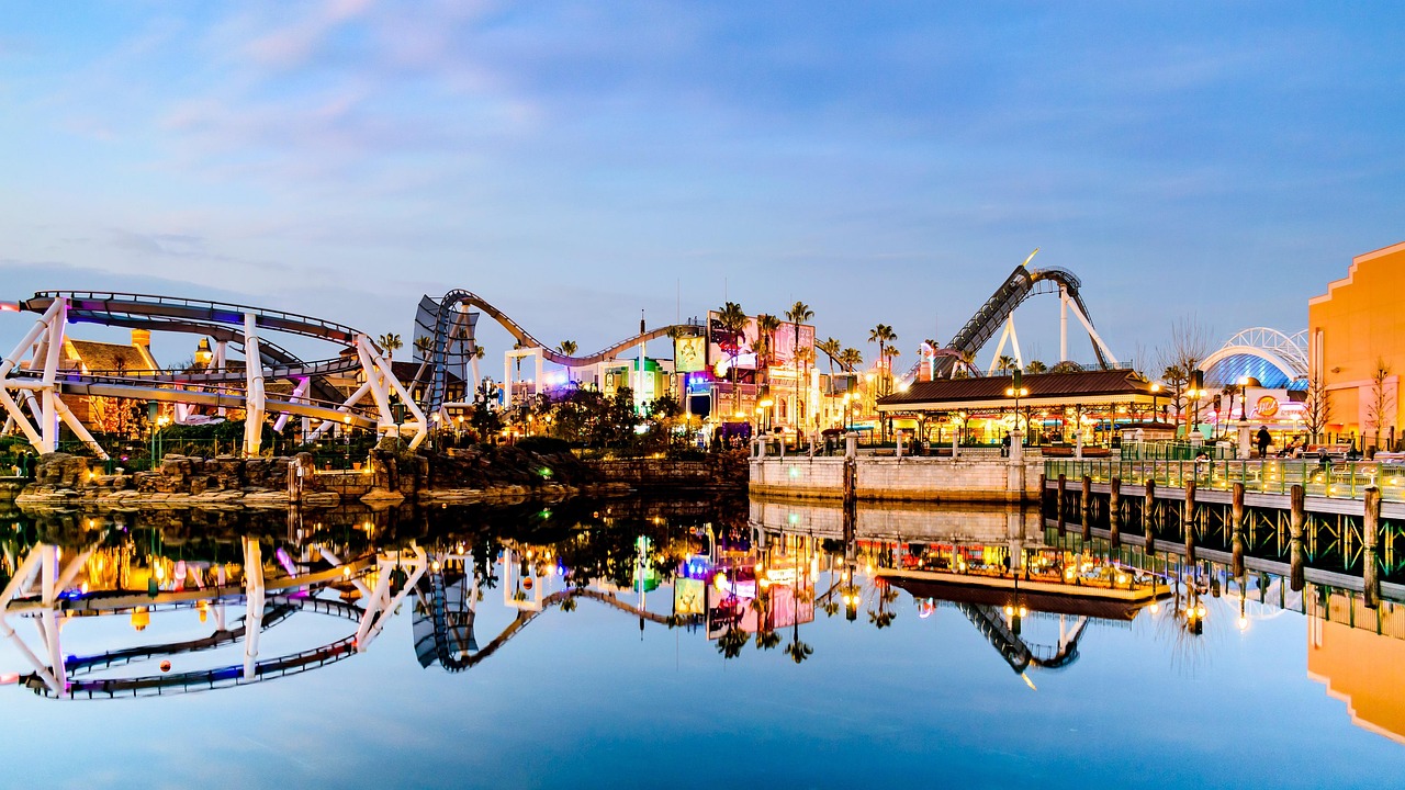 A theme park skyline of rollercoasters and lit buildings reflected in water at dusk.