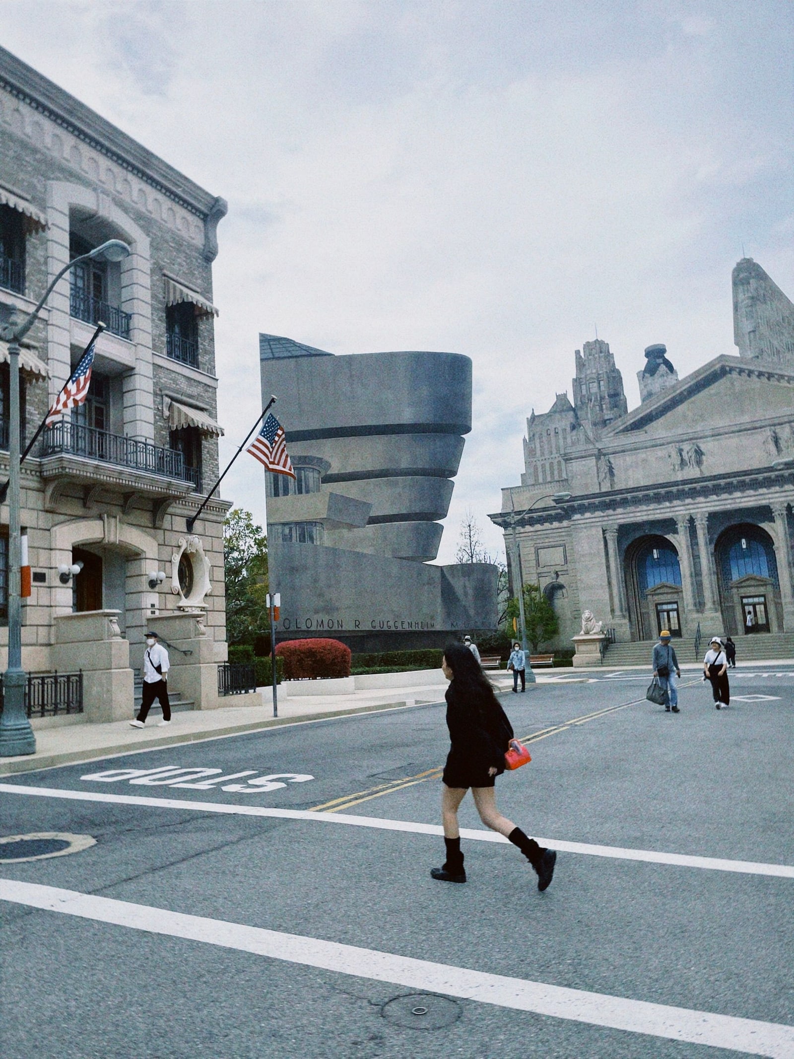A visitor crosses an empty backlot street between period-style building facades at a theme park.