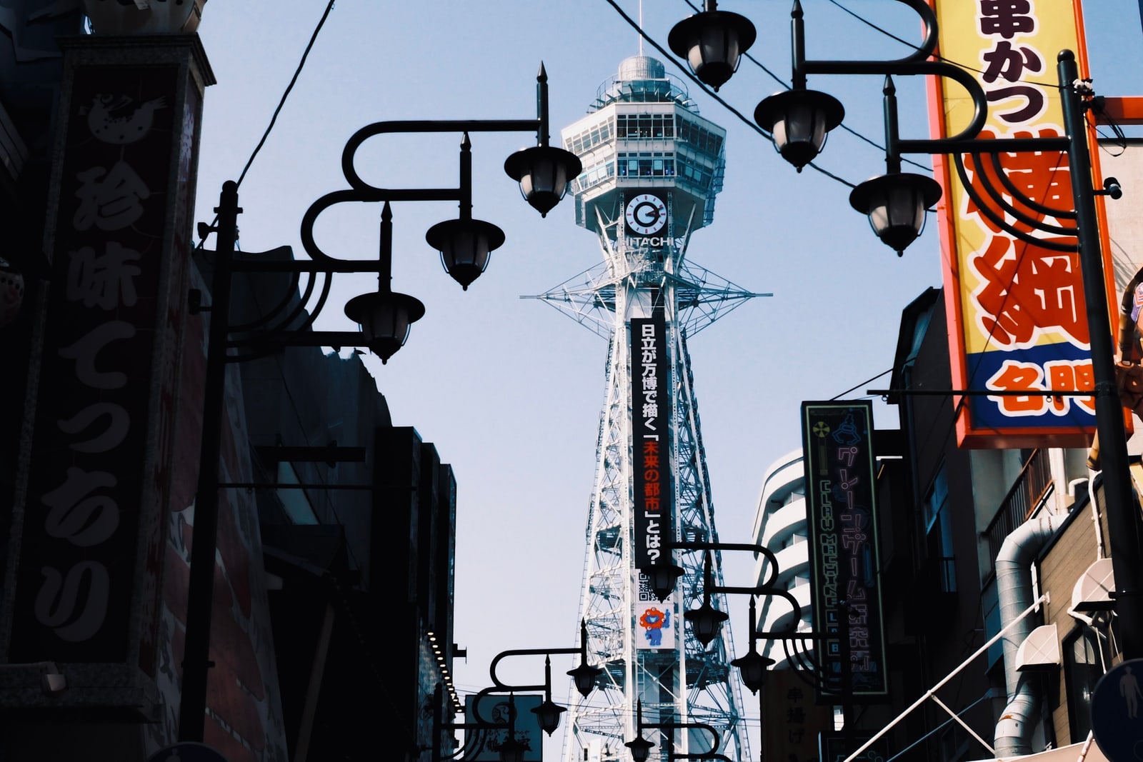 Tsutenkaku Tower rises above a street of shop signs and lanterns in Osaka's Shinsekai district.