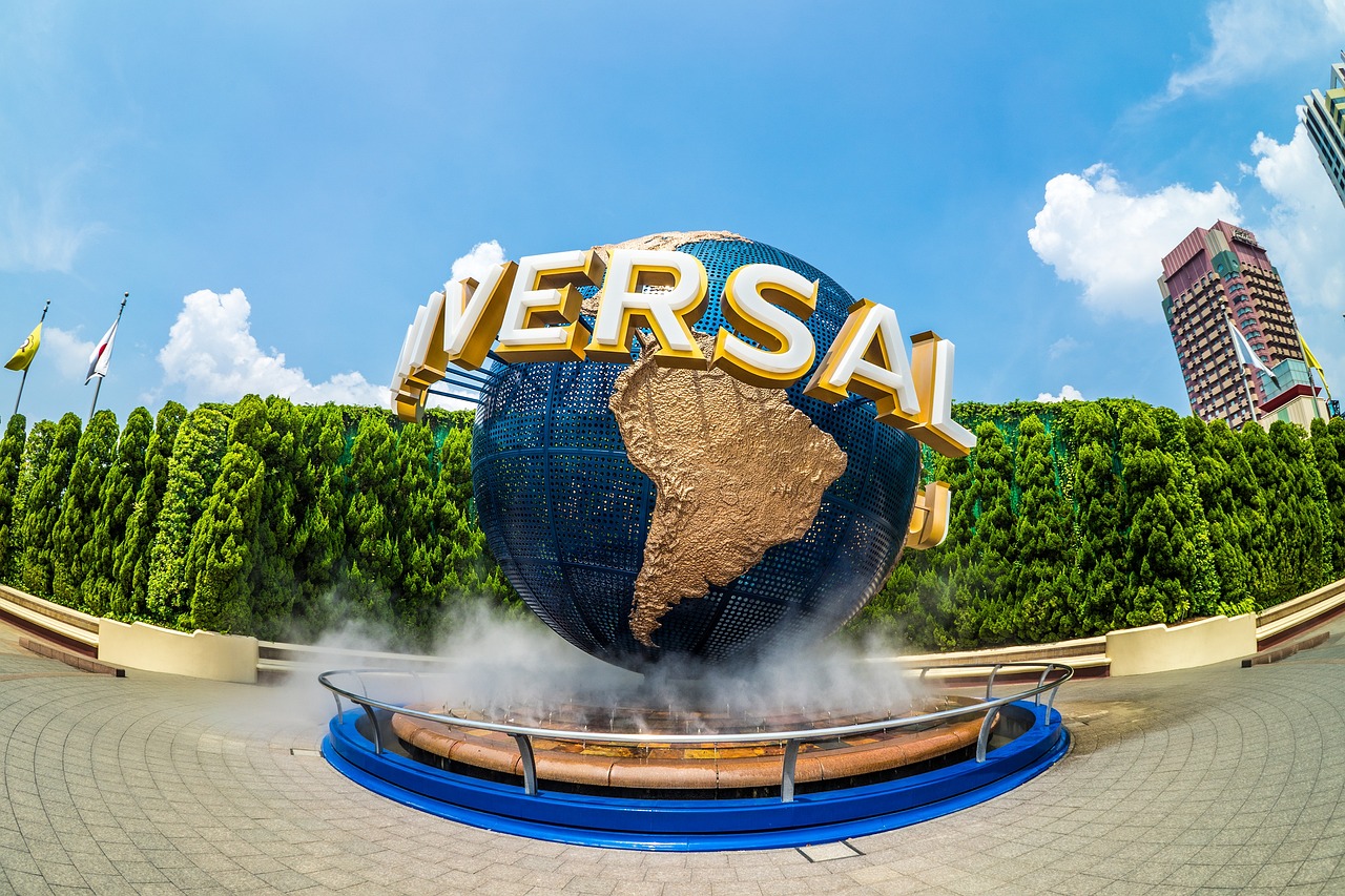 A wide-angle view of the rotating Universal globe fountain, with a Japanese flag and a hotel tower in the background.