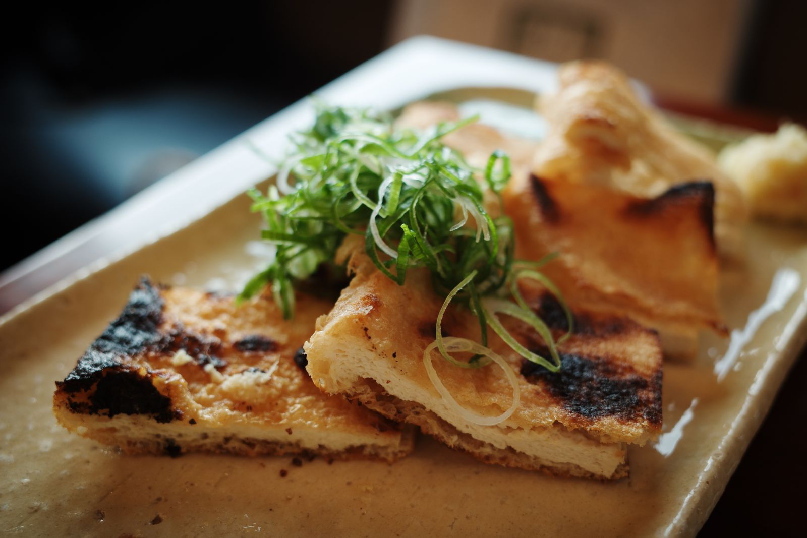 Slices of grilled fried tofu on a ceramic plate, heaped with sliced scallions and a small mound of grated ginger, in Kyoto.