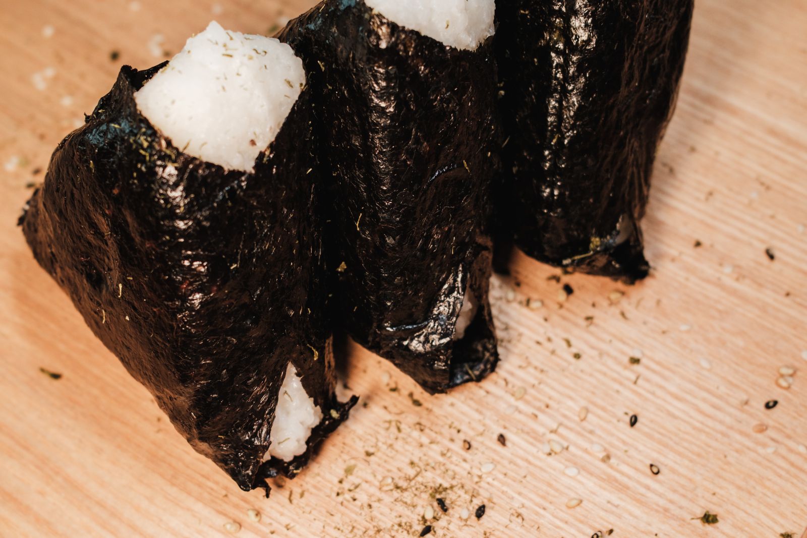 Three nori-wrapped onigiri, out of their packaging, on a wooden board.