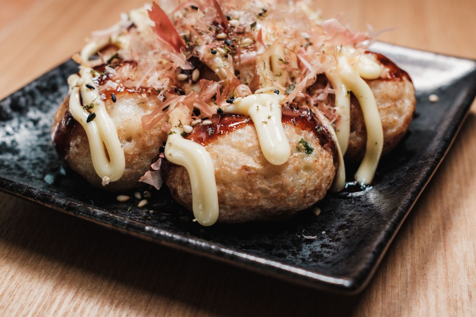 Takoyaki on a black plate, topped with mayonnaise and a layer of bonito flakes.