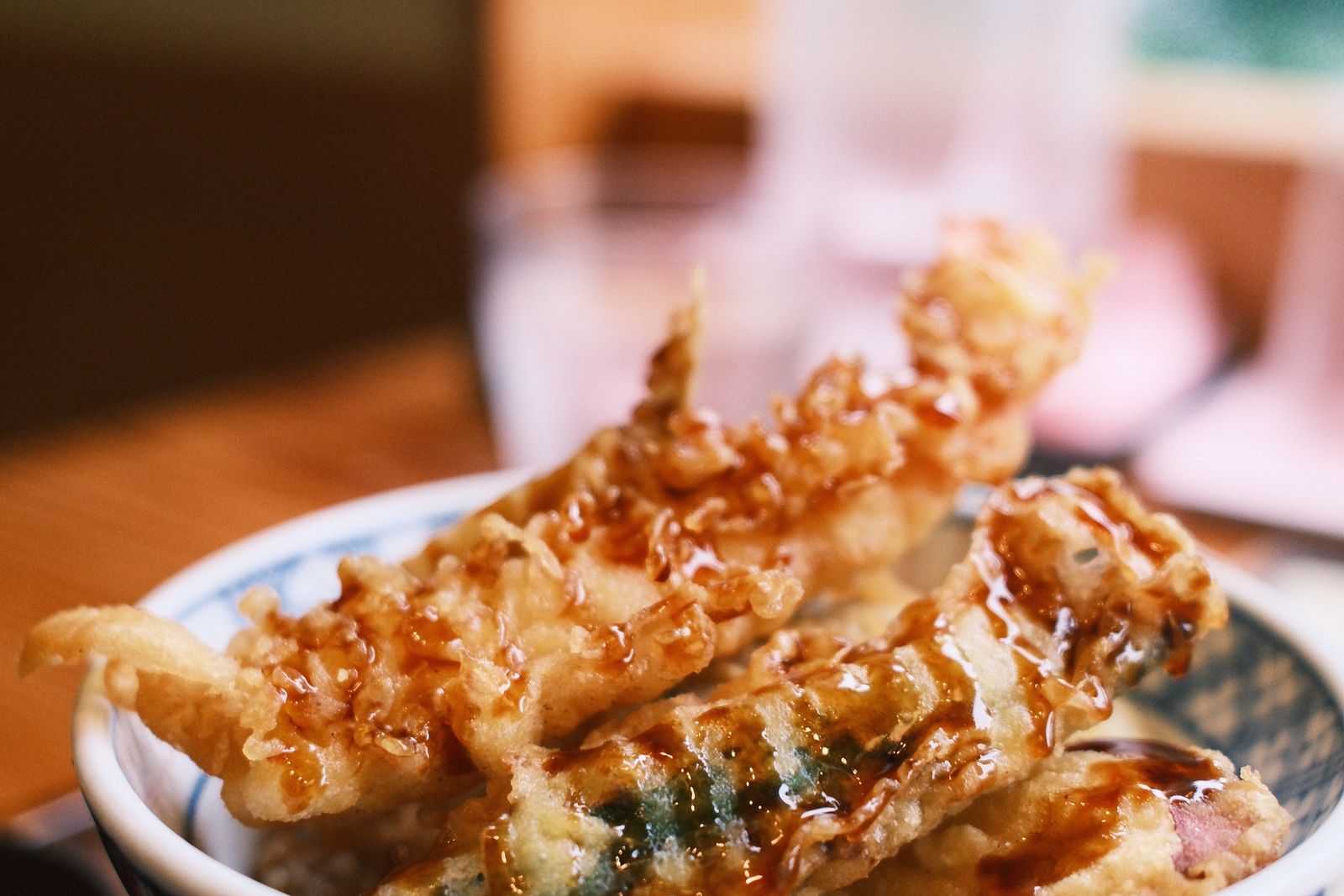 A bowl of shrimp and vegetable tempura over rice, a dark sauce poured over the top, on a table in Tokyo.