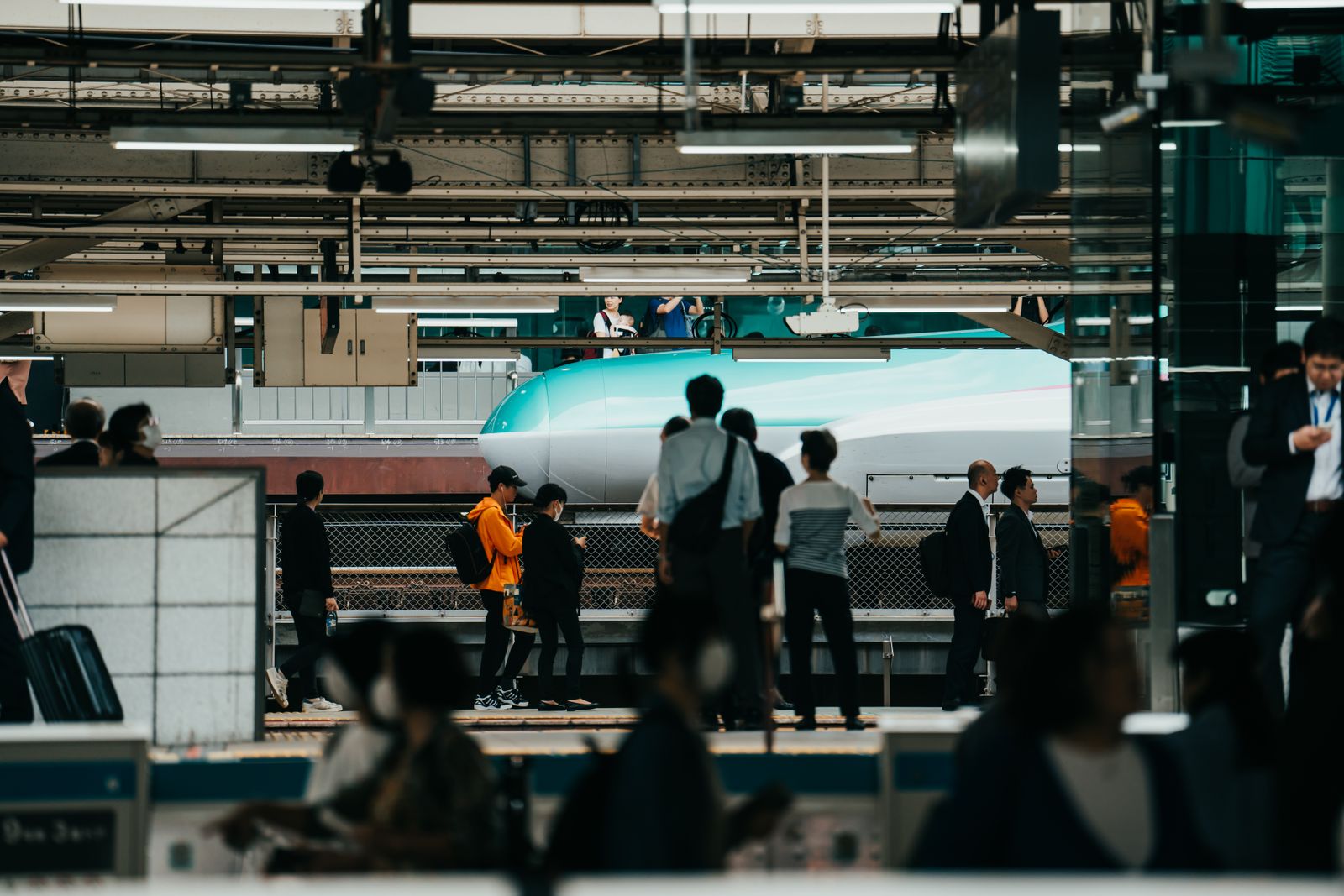 A crowded shinkansen platform in Japan, travelers layered across the frame with a green-nosed bullet train behind them.
