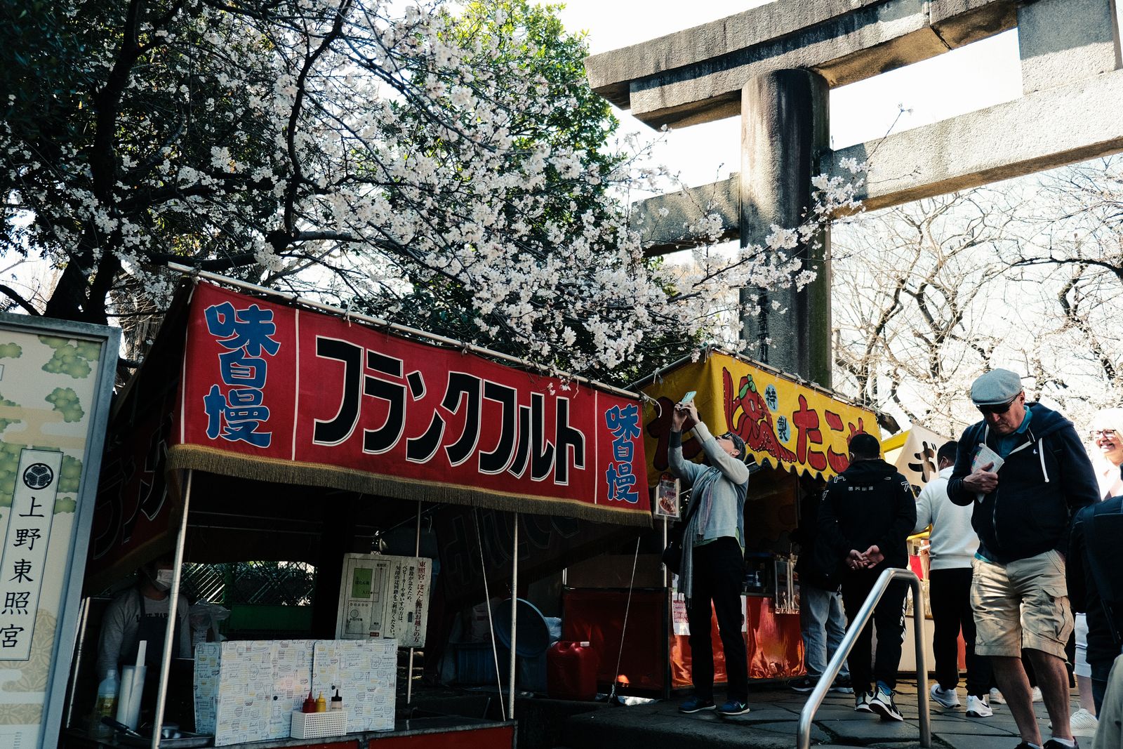 Blossom-season crowds and food stalls at the gate of Ueno Tōshōgū shrine.
