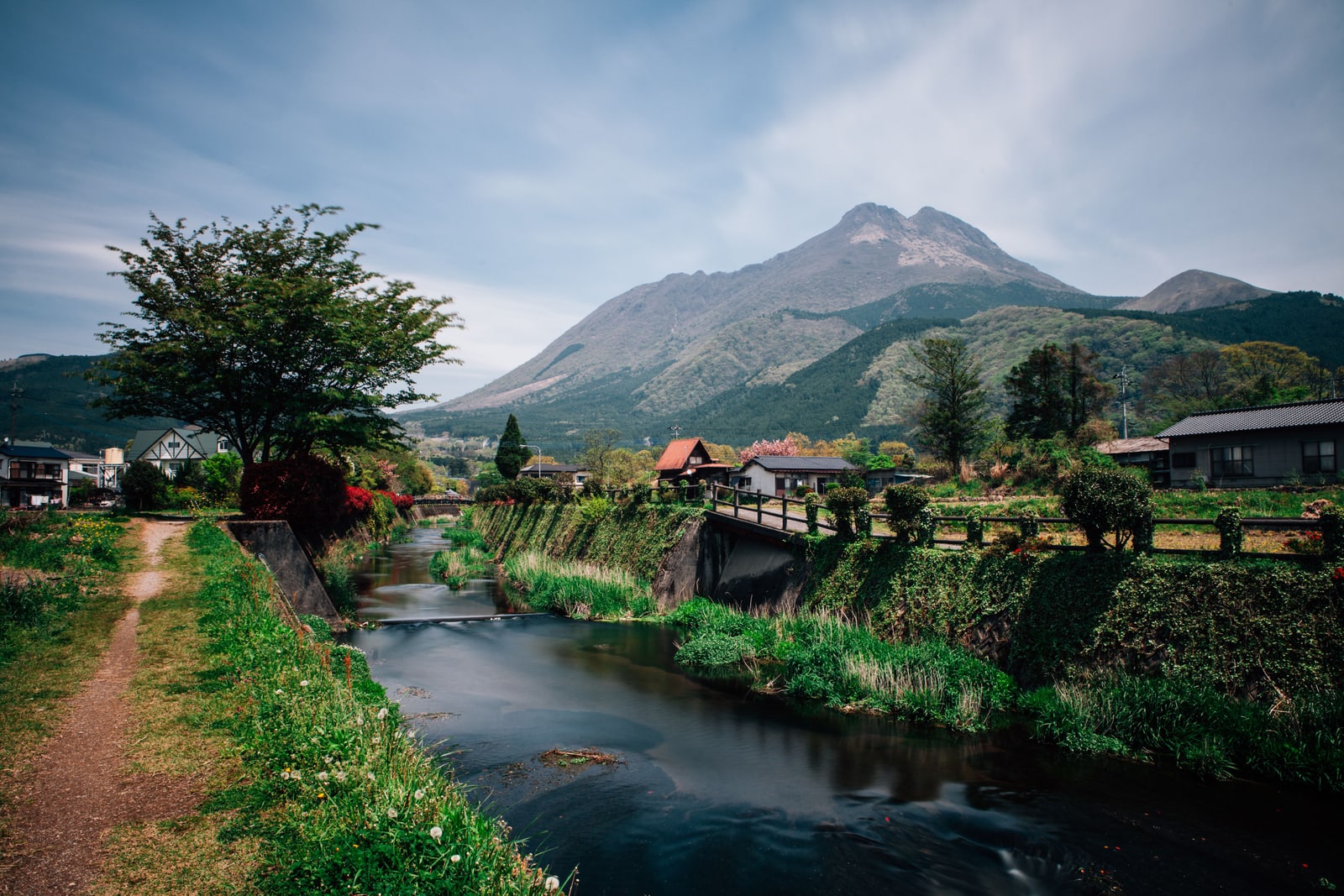 Twin-peaked Mt. Yufu above a stream and houses in spring green